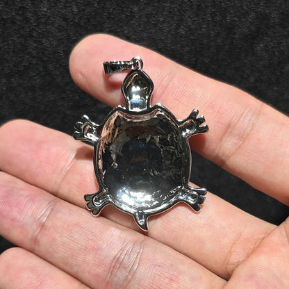 Back view comparison of 35mm sea turtle pendant showing silver tone alloy metal backing and bail loop held on hand