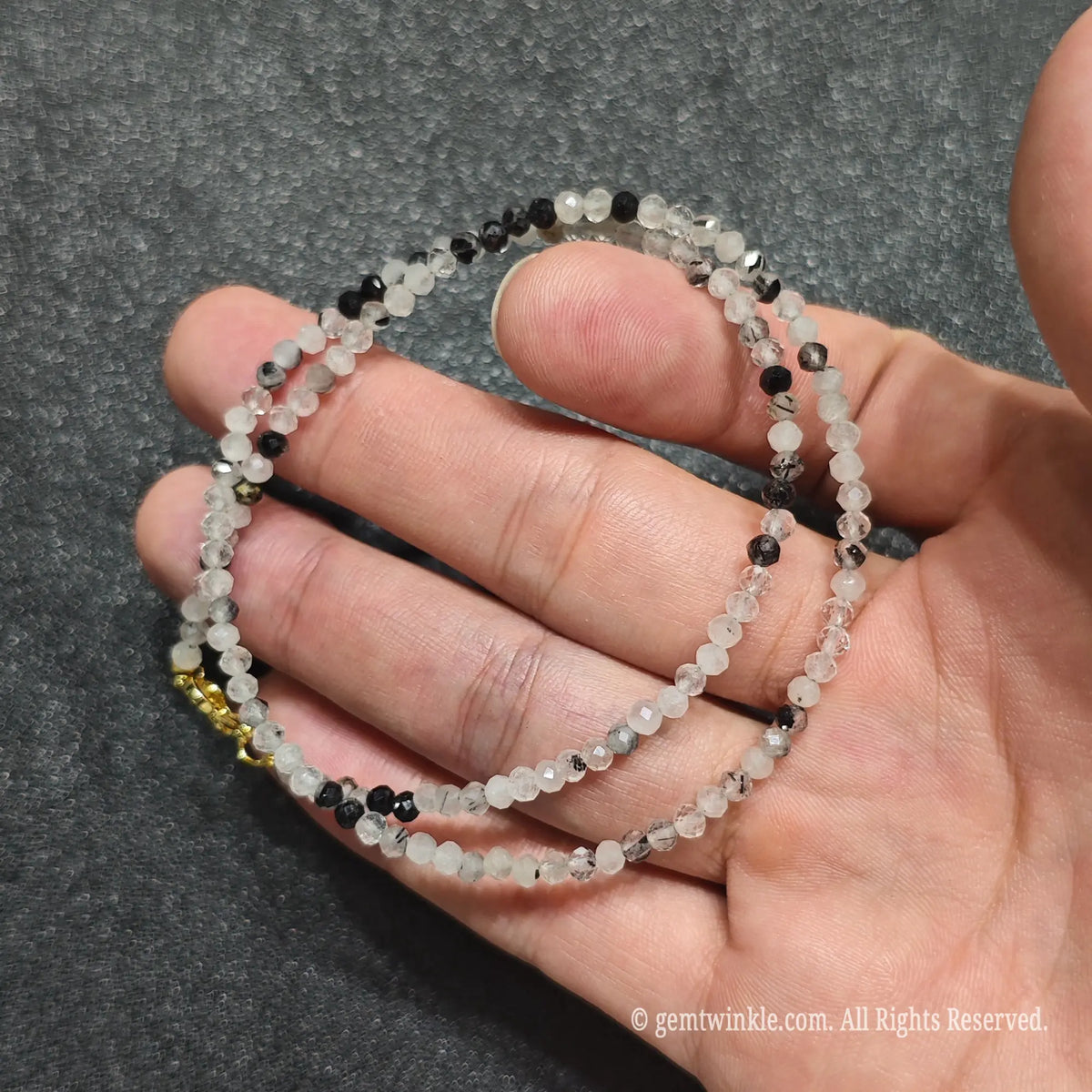 Close up of 3mm smoky black rutilated quartz beads held across fingers highlighting gold lobster clasp and extender
