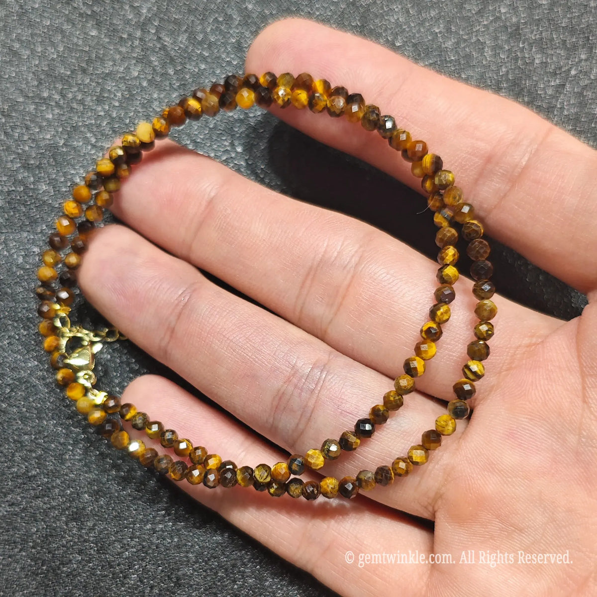Close up of 3mm Golden Tiger Eye beads looped on hand highlighting gold-plated lobster clasp and extension chain