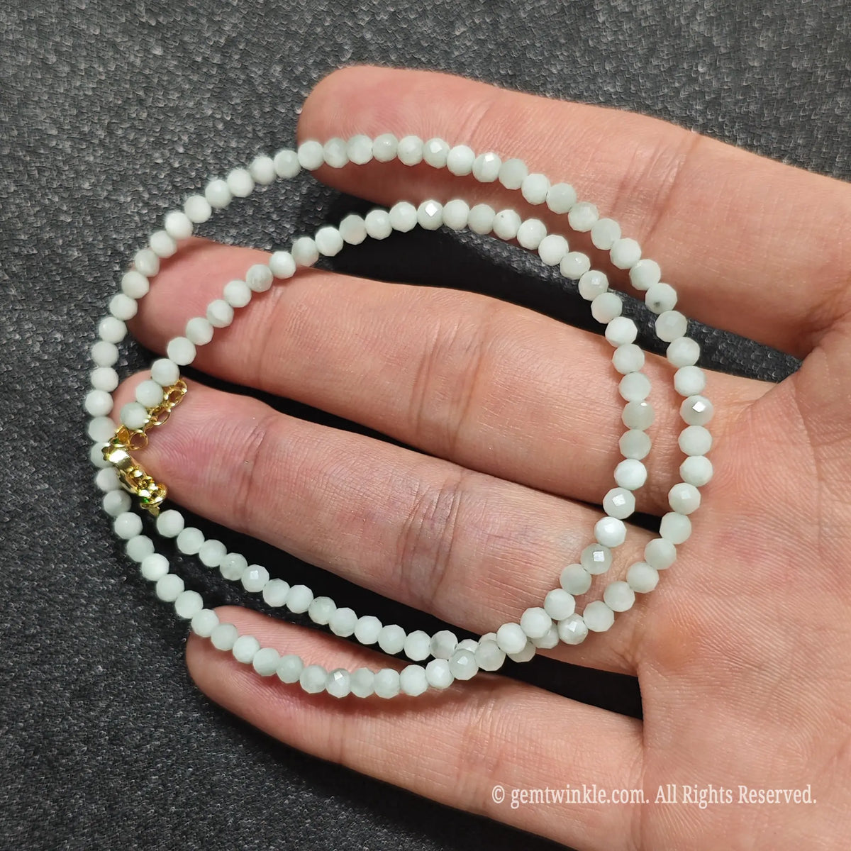 Close up of 3mm opaque green angelite beads held across fingers highlighting gold lobster clasp and extender