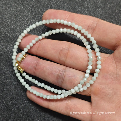 Close up of 3mm opaque green angelite beads held across fingers highlighting gold lobster clasp and extender