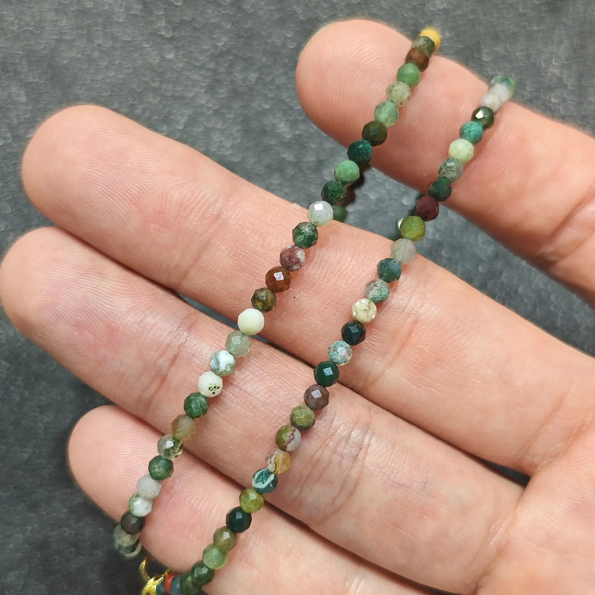 Close up of 3mm micro faceted ocean jasper beads held across fingers highlighting gold extender chain