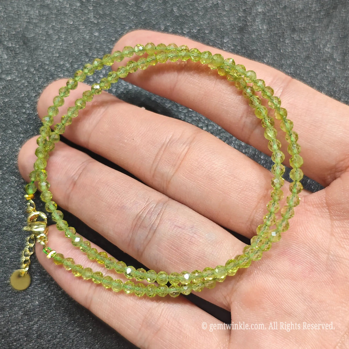 Close up of 3mm faceted green peridot beads looped on hand highlighting gold-plated lobster clasp and extender