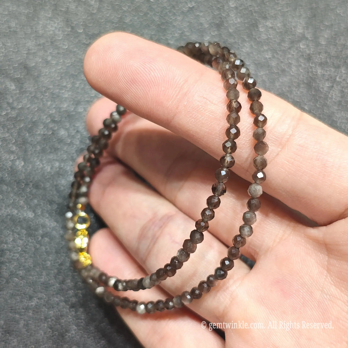 Close up of 3mm Silver Sheen Obsidian beads looped on hand highlighting gold-plated lobster clasp and extender