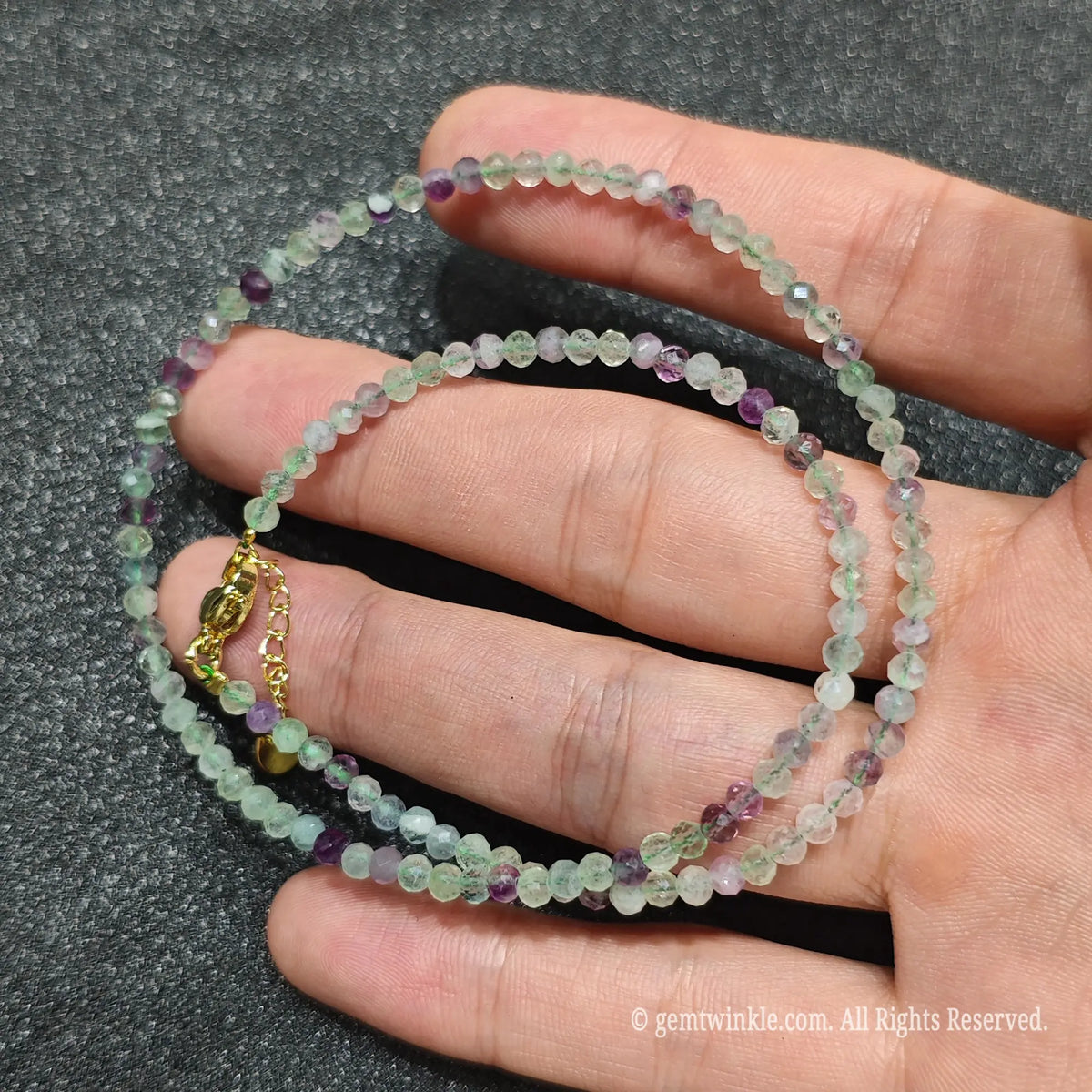 Close up of 3mm micro faceted rainbow fluorite beads looped on hand highlighting gold extension chain