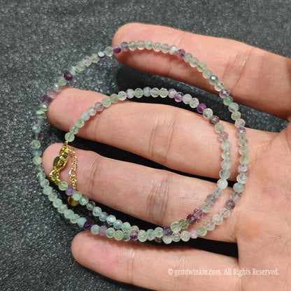 Close up of 3mm micro faceted rainbow fluorite beads looped on hand highlighting gold extension chain