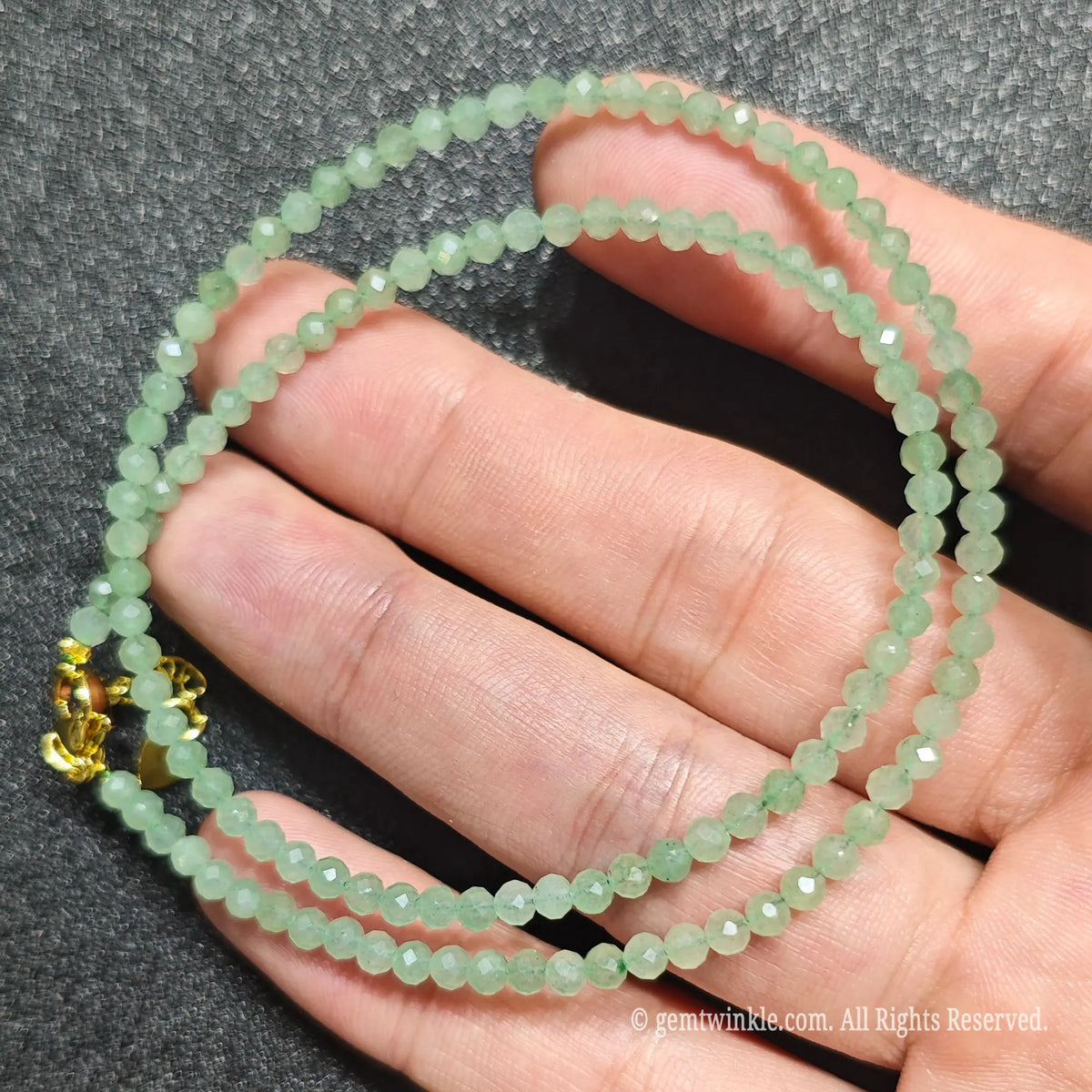 Close up of 3mm micro faceted green aventurine beads looped on hand highlighting gold extension chain