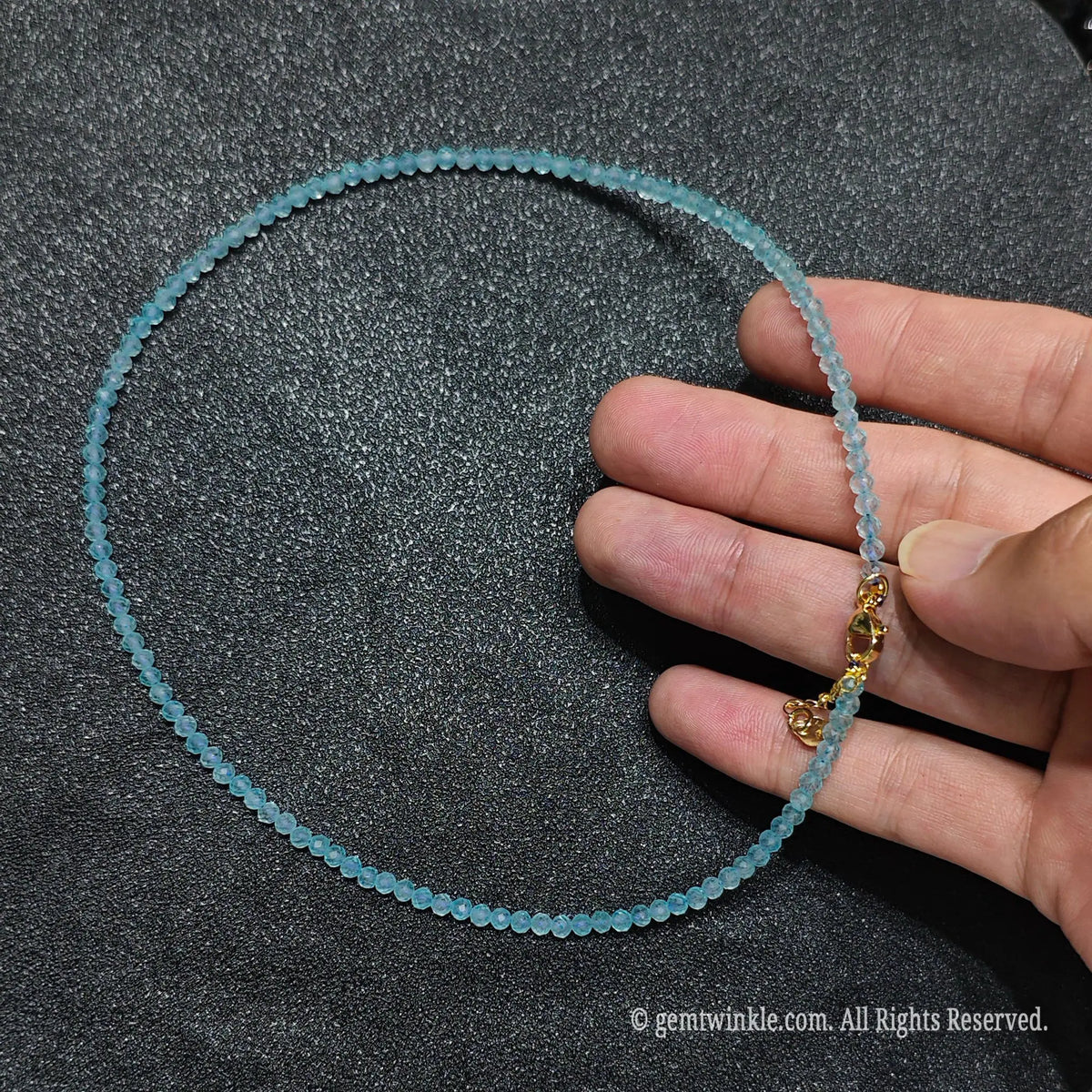 Hand holding 3mm faceted sky blue topaz beaded necklace showcasing crystal clarity and gold lobster clasp