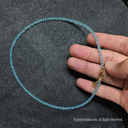 Hand holding 3mm faceted sky blue topaz beaded necklace showcasing crystal clarity and gold lobster clasp