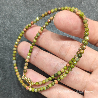 Close up of 3mm micro faceted unakite beads looped on hand highlighting gold extension chain