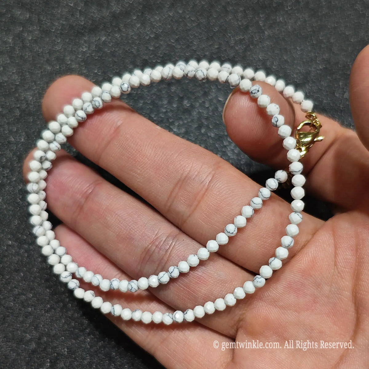 Close up of 3mm micro faceted white howlite beads looped on hand highlighting gold extension chain
