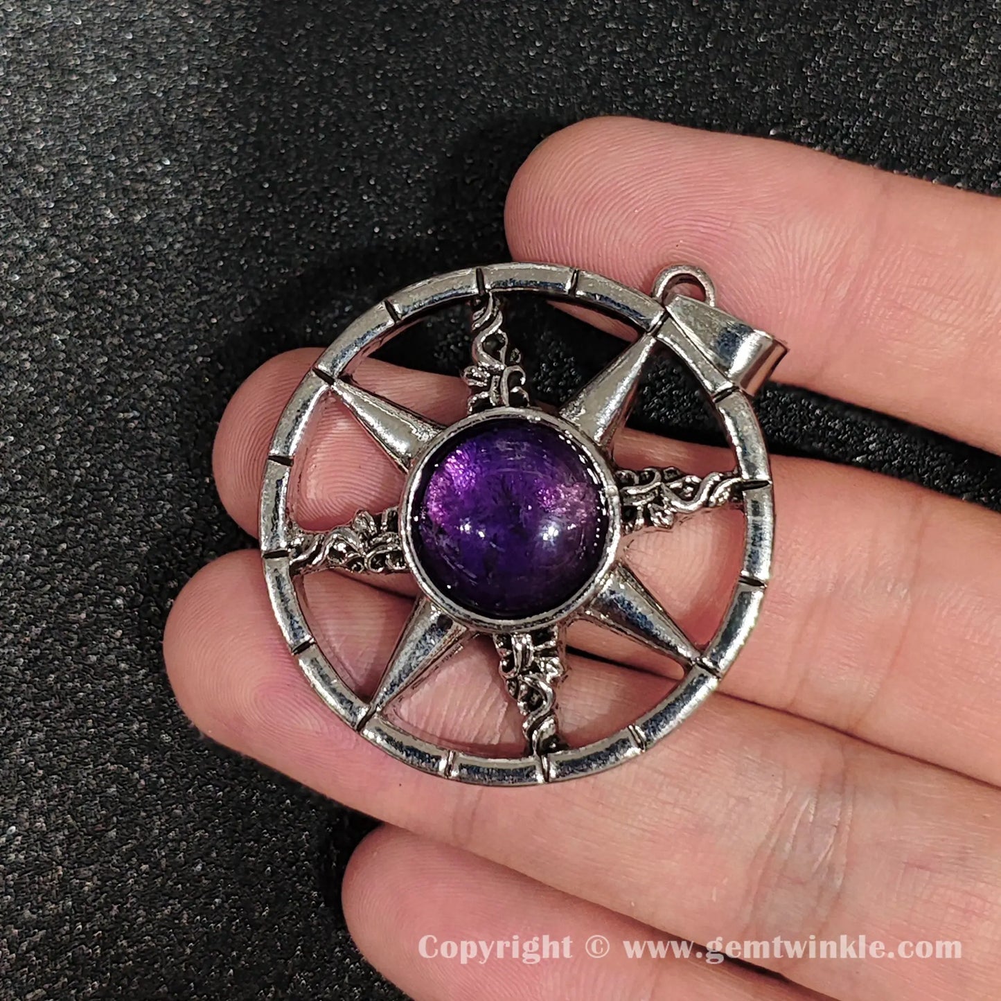 Handheld view of 45mm metal alloy eight pointed sunburst star pendant showing natural amethyst inclusions