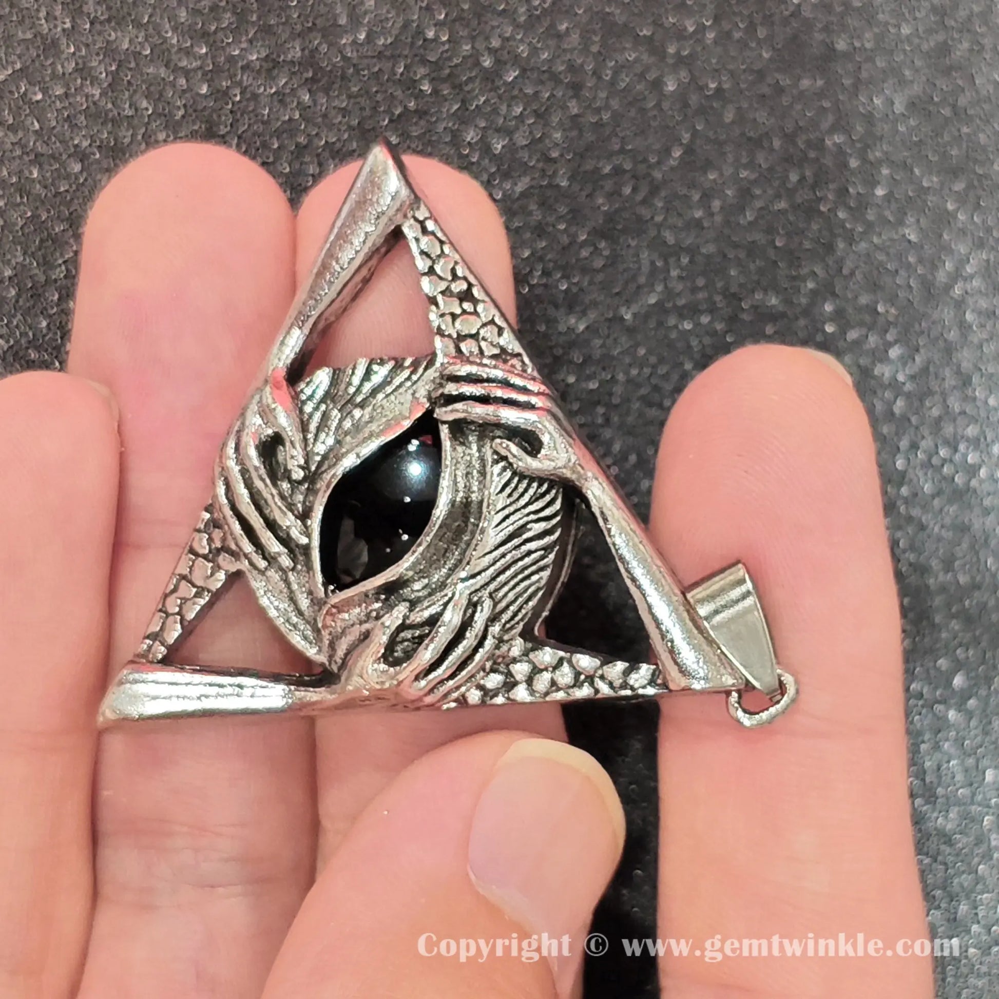 Handheld perspective showing 45mm dark obsidian triangle pendant with carved hand details