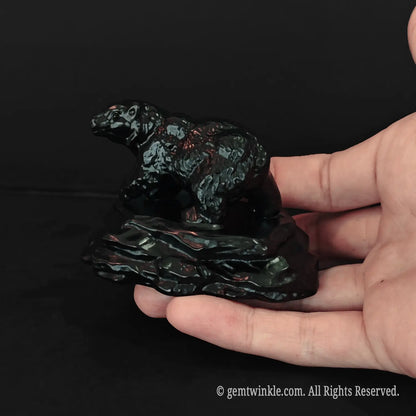 human hand holding an eight centimeter black obsidian bear statue to show real scale