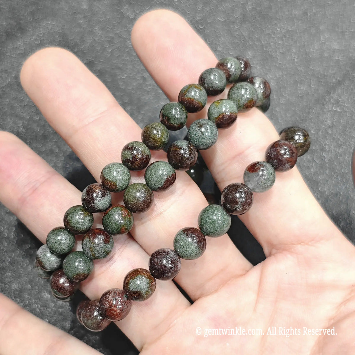 Fingertips holding a multi-colored red and green chlorite quartz stretch bracelet showcasing earthy inclusions
