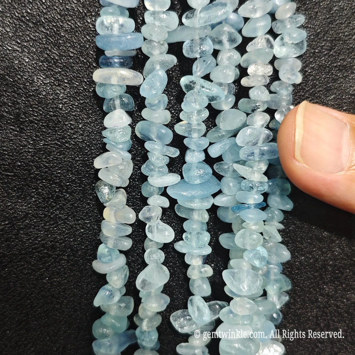 Close up of multi strands of acid-washed aquamarine 5-10mm irregular light blue chips