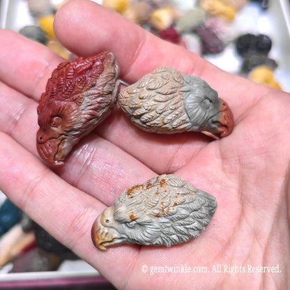 Palm displaying multiple natural Alxa agate eagle head mini sculptures in varied gray brown and red tones