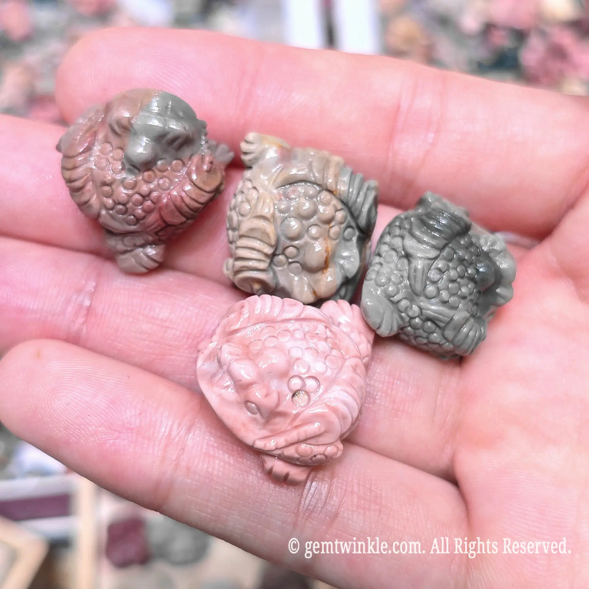 Palm holding multiple natural Alxa agate money toad mini sculptures in assorted gray pink and green earthy shades