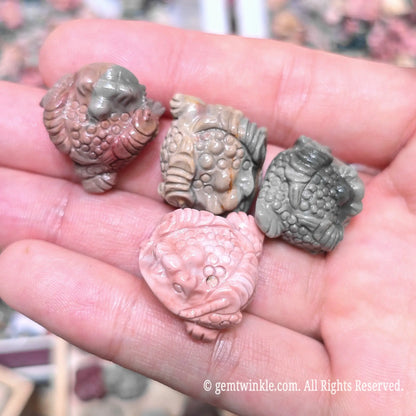Palm holding multiple natural Alxa agate money toad mini sculptures in assorted gray pink and green earthy shades