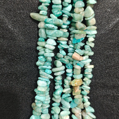Fingers holding shimmering natural amazonite gemstone chip beads on black background