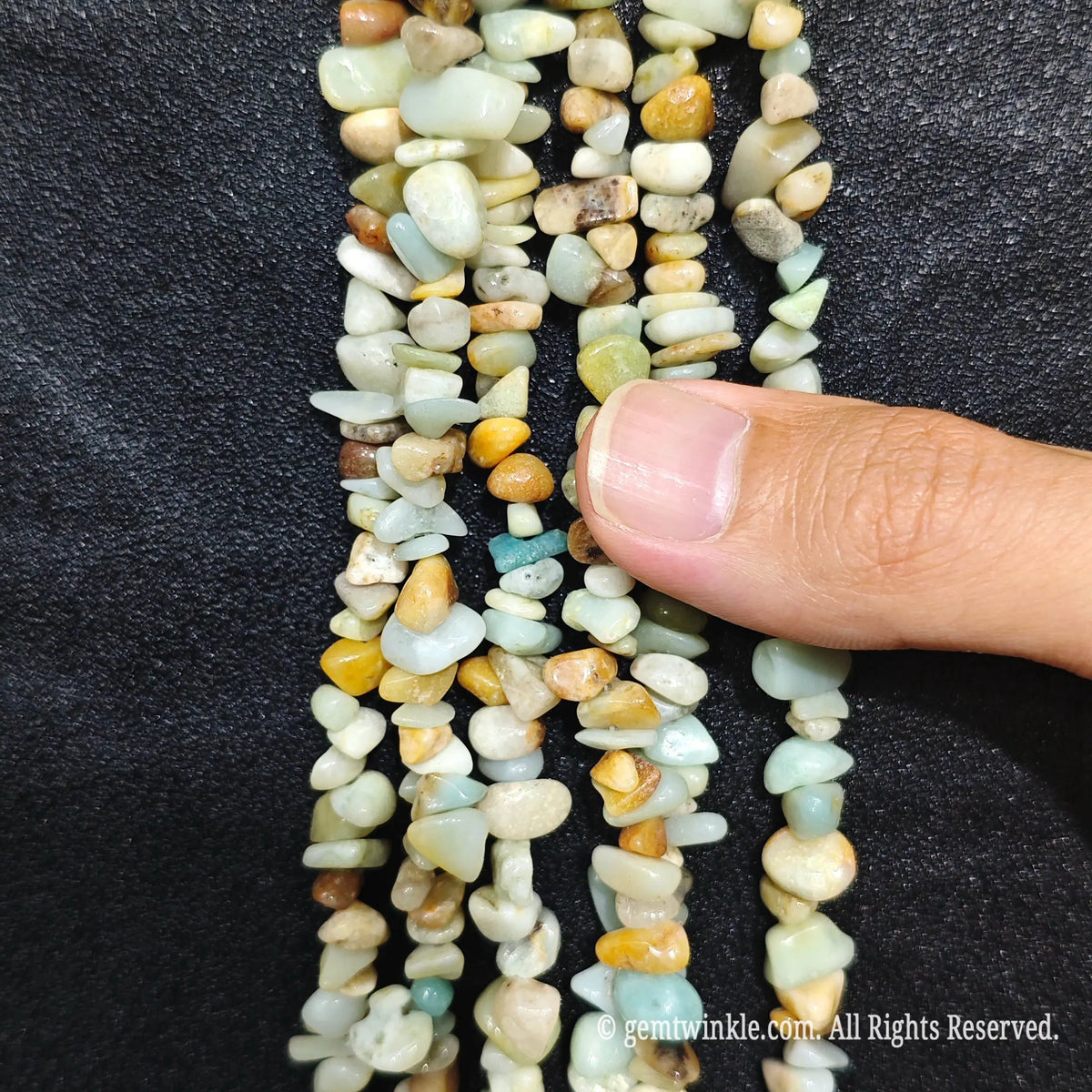 Close up hand holding natural amazonite stone chips displaying polished blue-green surfaces with fine drill holes[cite: 6]