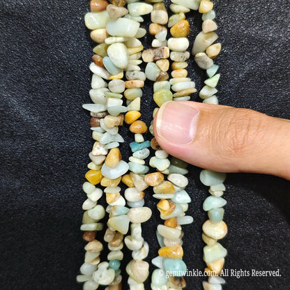 Close up hand holding natural amazonite stone chips displaying polished blue-green surfaces with fine drill holes[cite: 6]