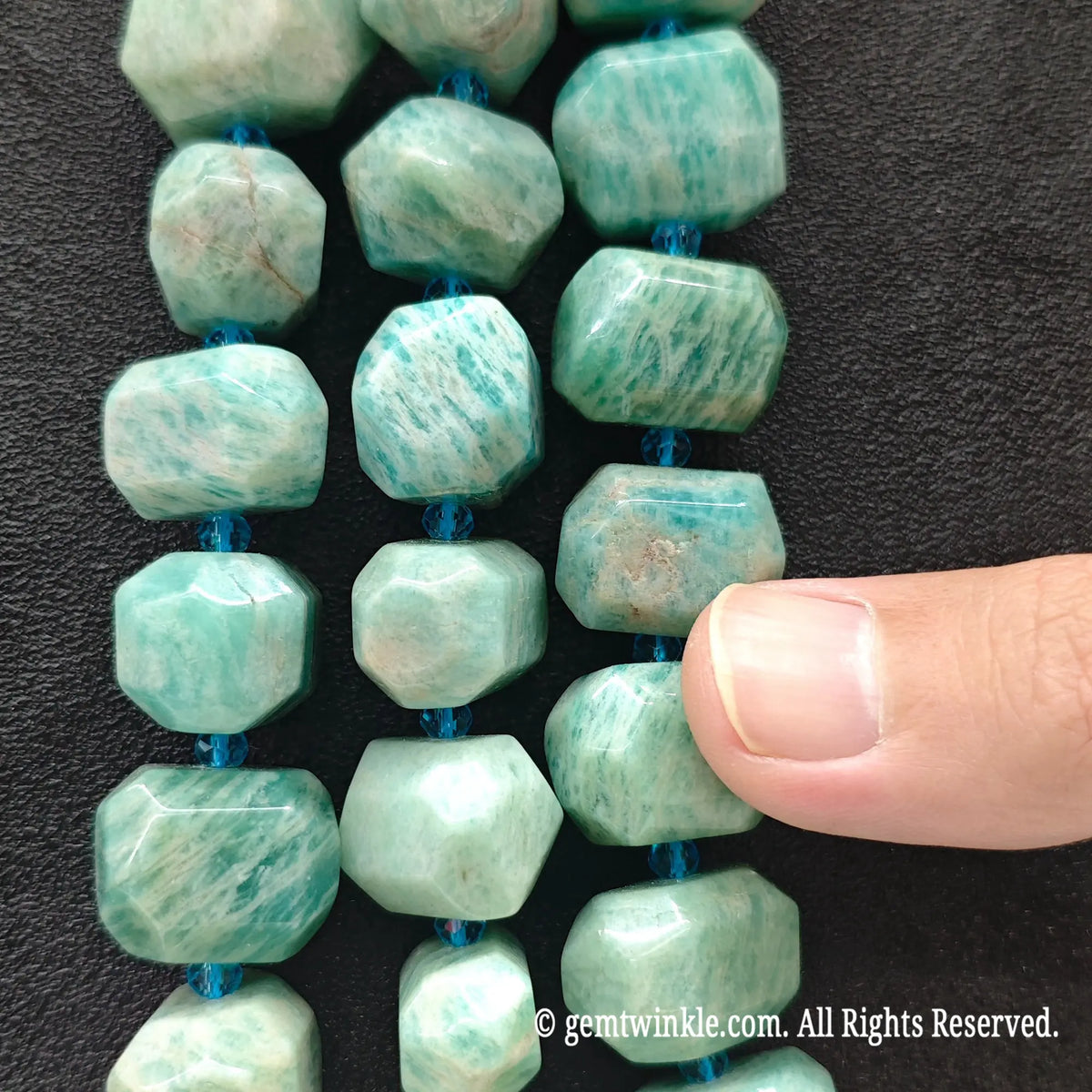 Finger pointing to a large natural amazonite freeform faceted bead displaying natural white matrix and mint color