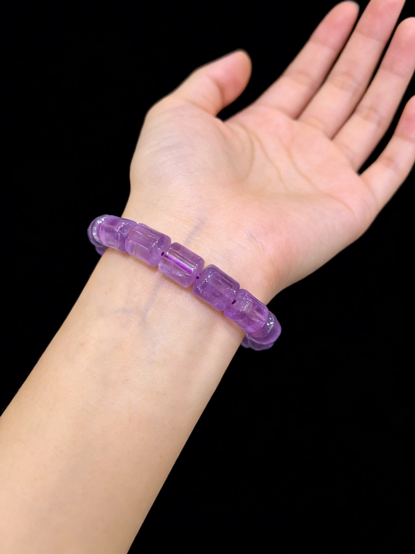 Light purple amethyst crystal bracelet worn on a person’s wrist against a black background, showcasing its fit, elasticity, and subtle translucency.