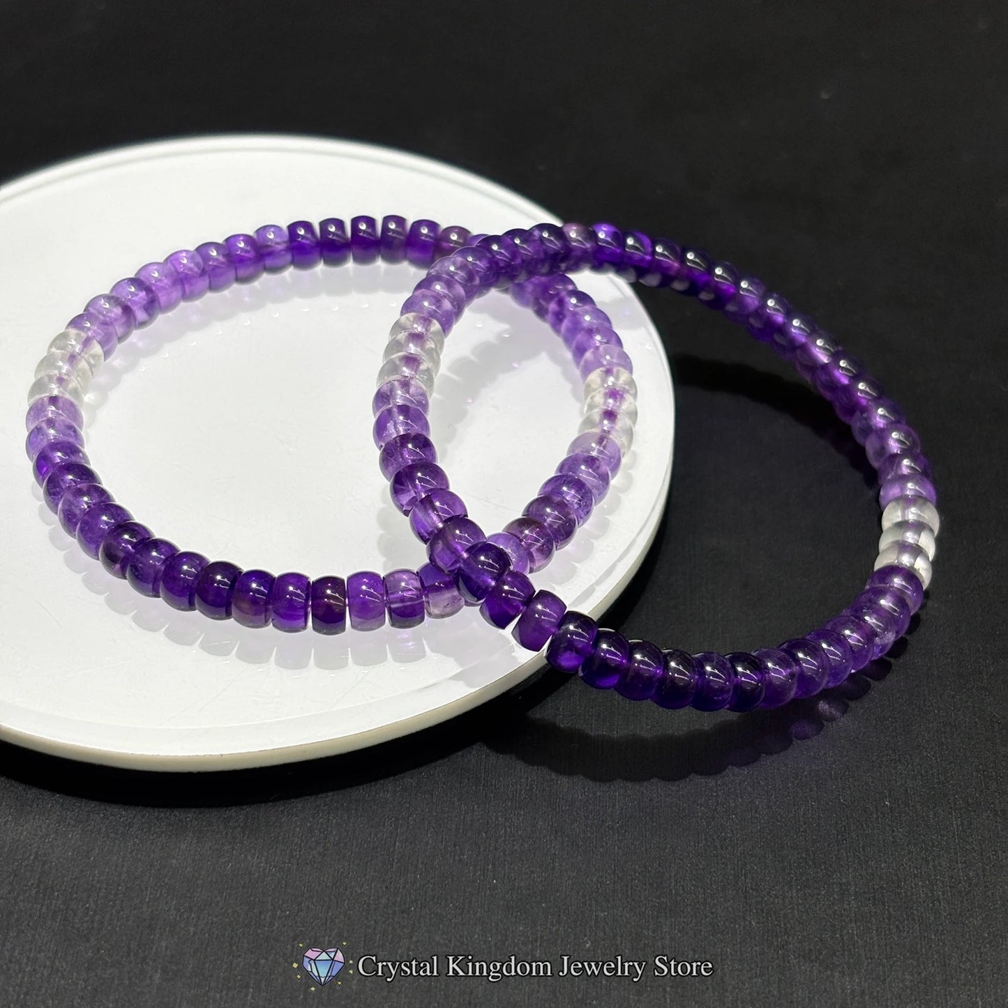 Close-up of stacked amethyst and clear quartz bead bracelets on white plate; highlights natural stone texture and color gradient