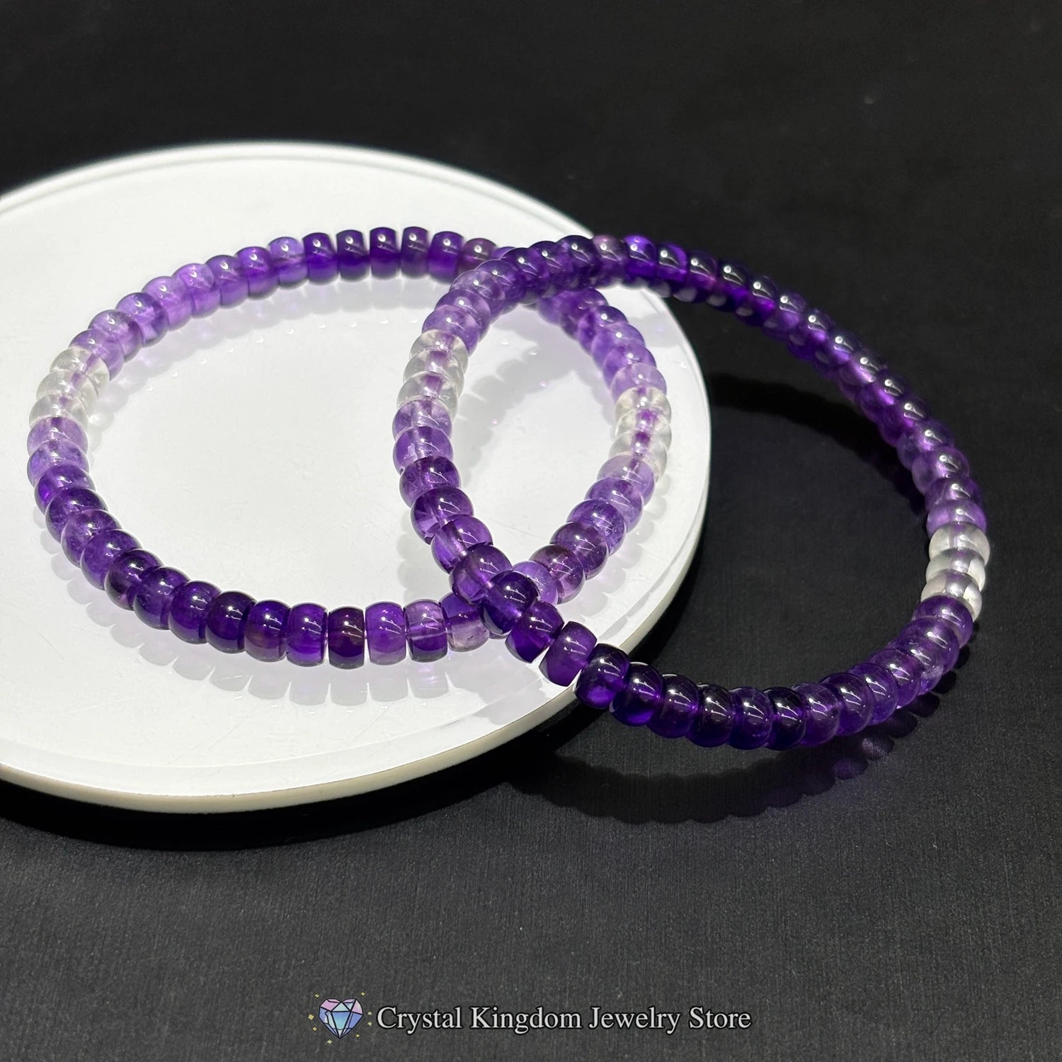 Close-up of stacked amethyst and clear quartz bead bracelets on white plate; highlights natural stone texture and color gradient