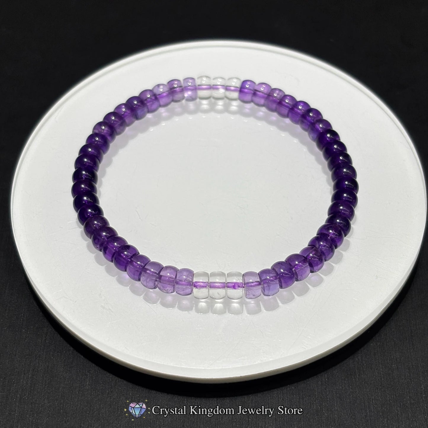 Top-down view of natural amethyst disc bead bracelet on white ceramic dish; showcases even bead spacing, purple gradient, and elastic stretch design
