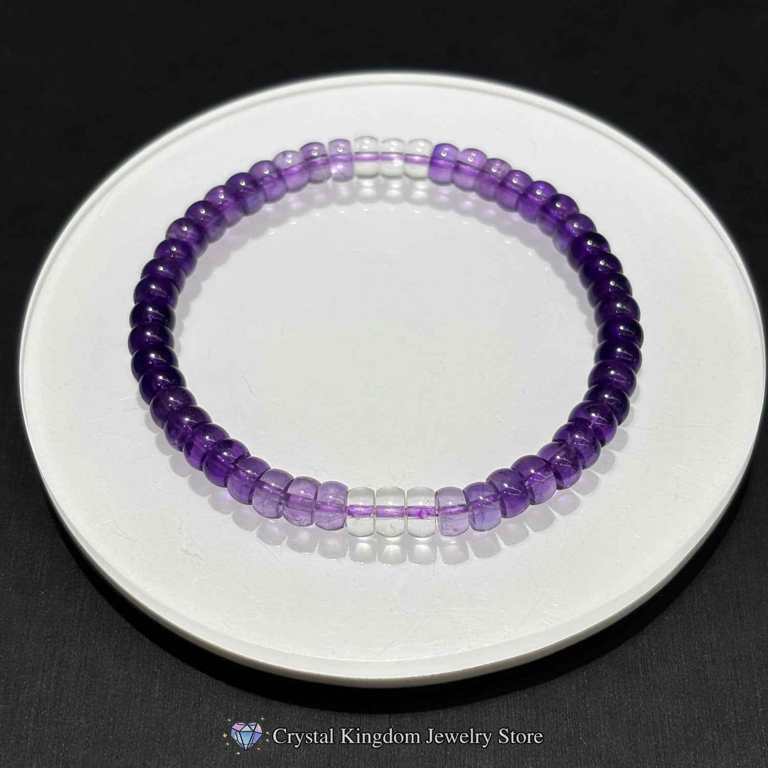 Top-down view of natural amethyst disc bead bracelet on white ceramic dish; showcases even bead spacing, purple gradient, and elastic stretch design