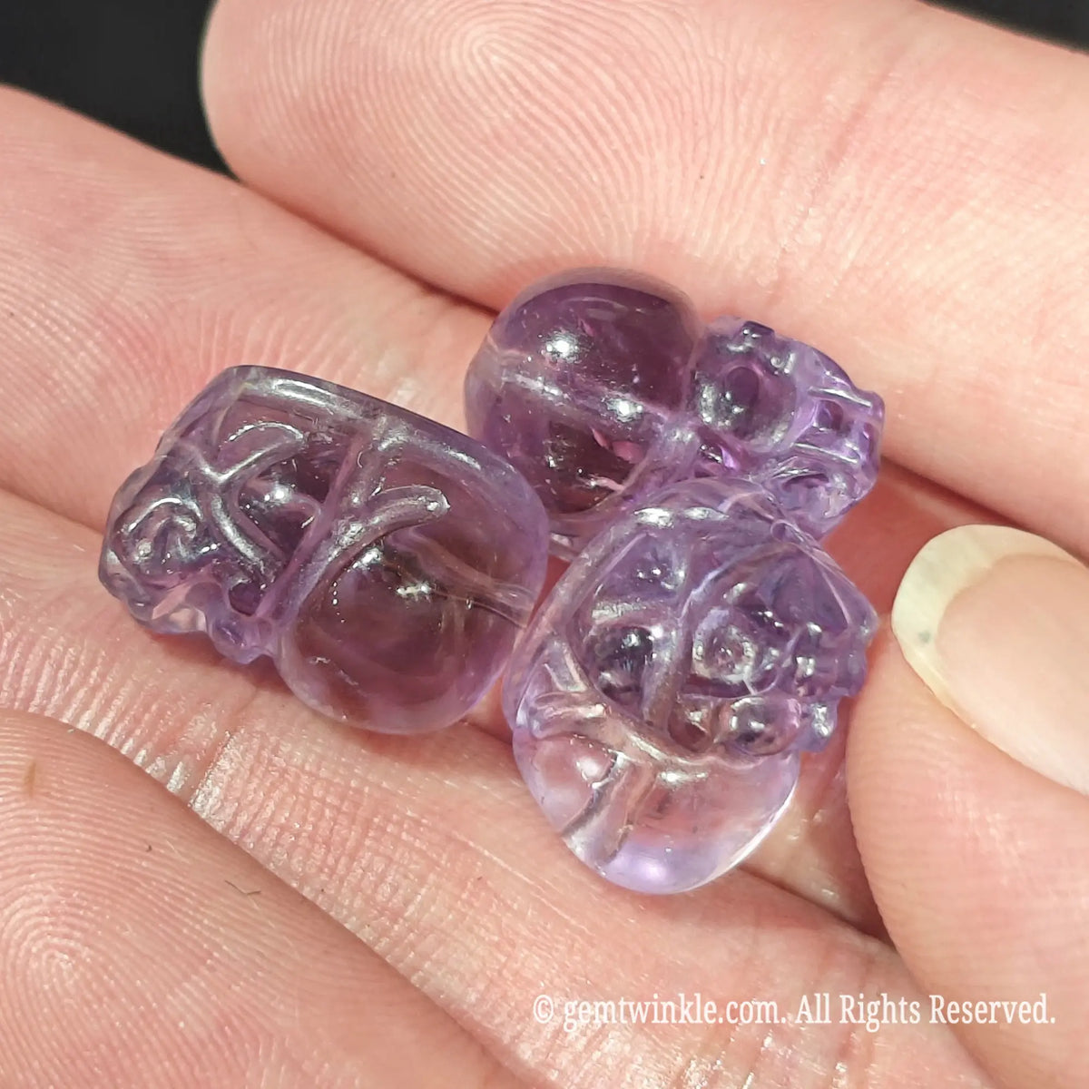 Palm displaying multiple natural purple amethyst Pixiu carved beads with pre-drilled center holes for jewelry making