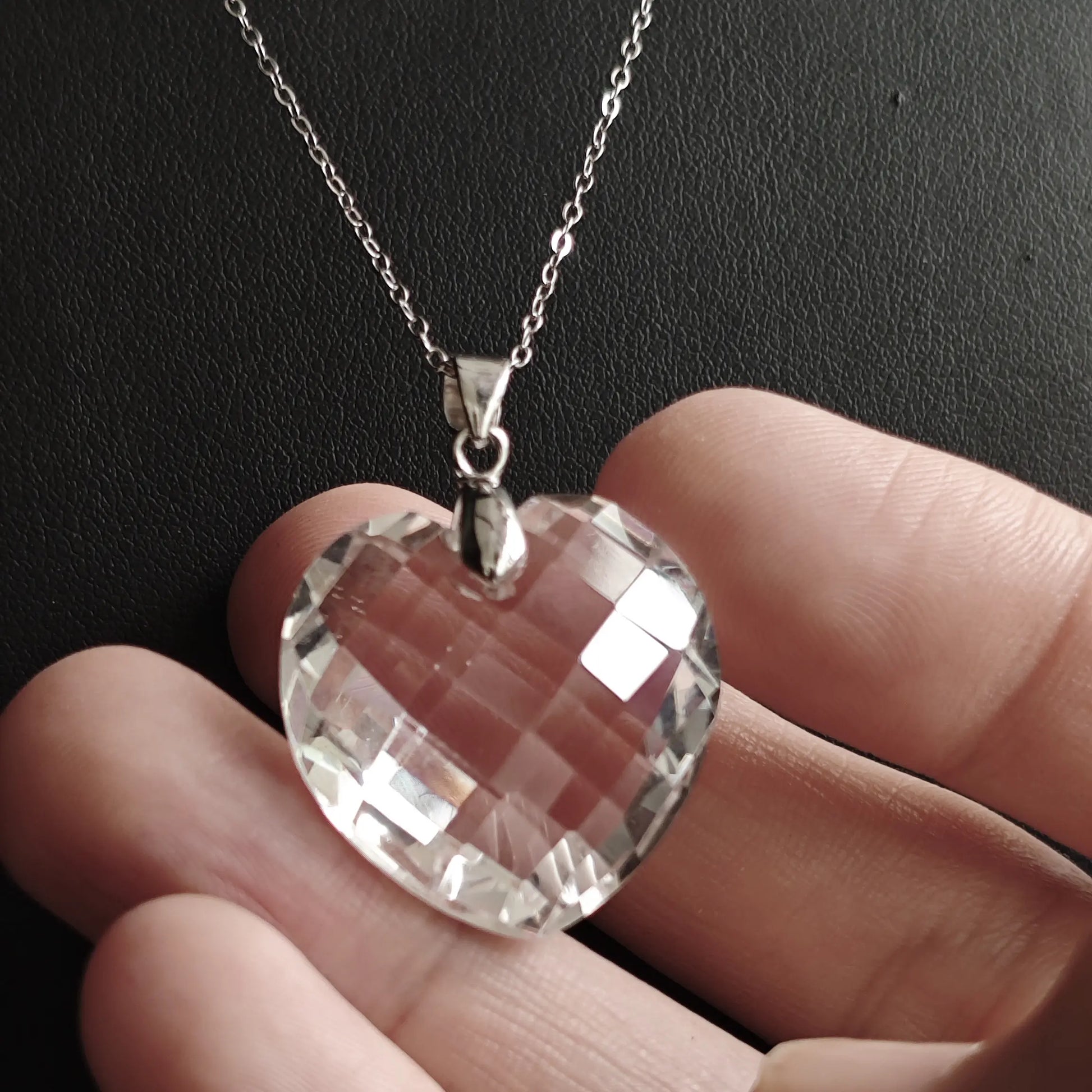 Angled close-up of clear quartz heart pendant in hand, capturing dynamic sparkle from faceted surfaces and natural inclusions