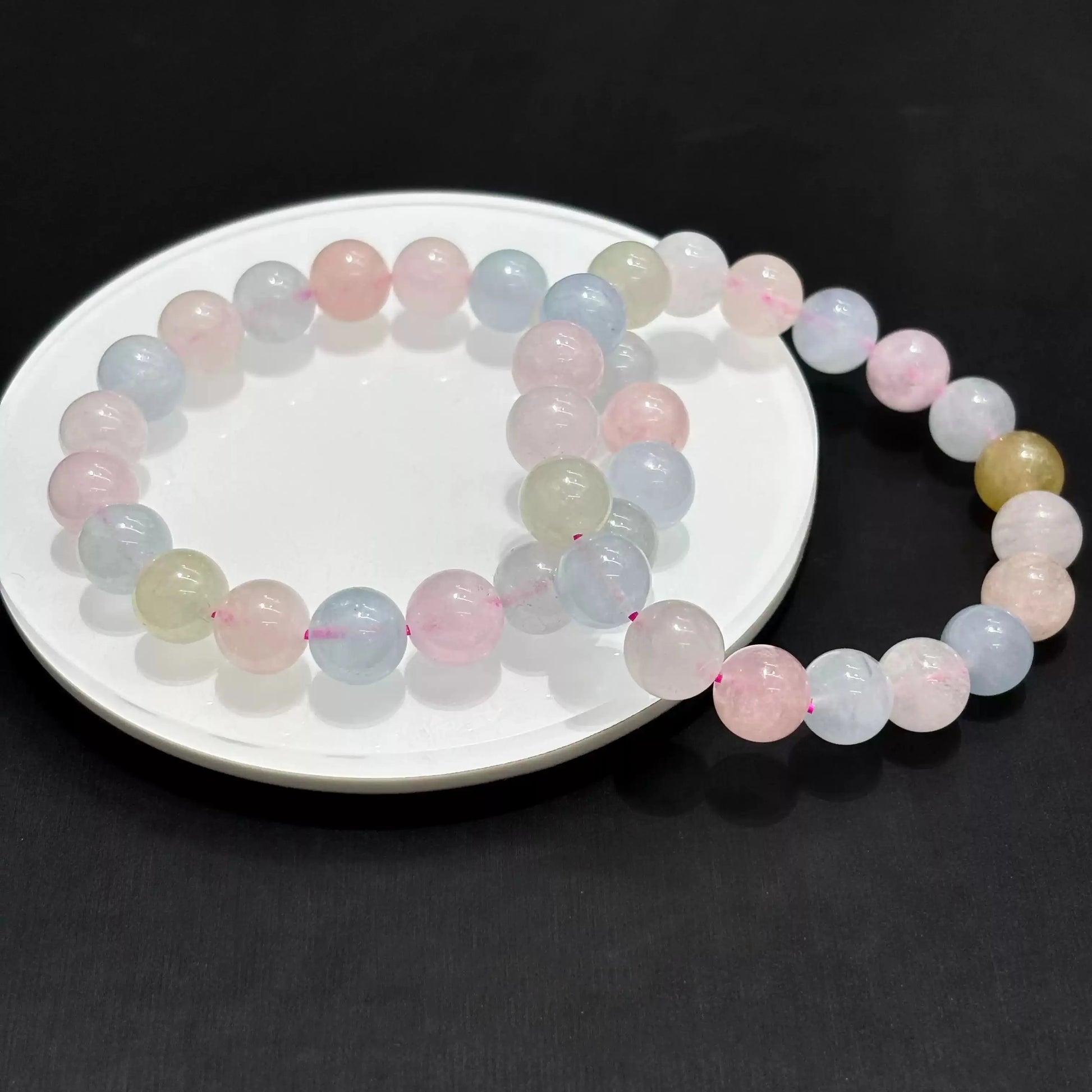 Morganite bracelet arranged in overlapping circles on white dish, highlighting bead uniformity and gentle color gradient.