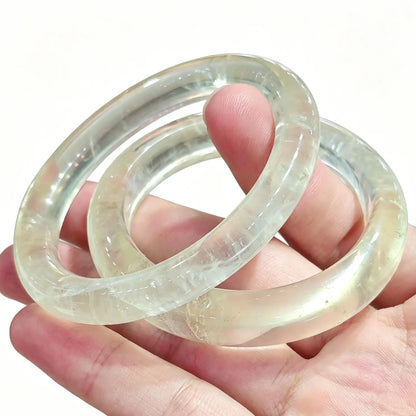 Pair of translucent lemon yellow quartz crystal bangles held in hand showing smooth inner ring polish