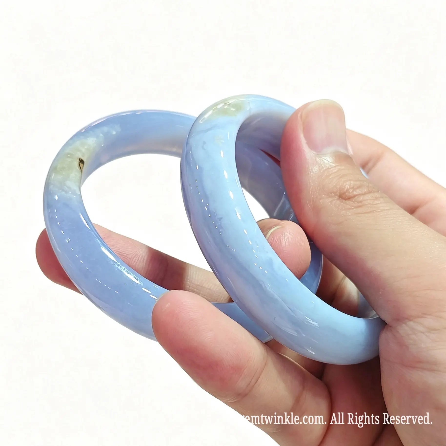 Close up view of blue lace agate solid bangles held in hand displaying subtle yellow druzy geode pockets and high gloss finish