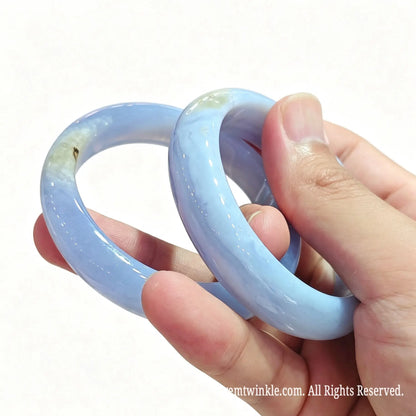 Close up view of blue lace agate solid bangles held in hand displaying subtle yellow druzy geode pockets and high gloss finish