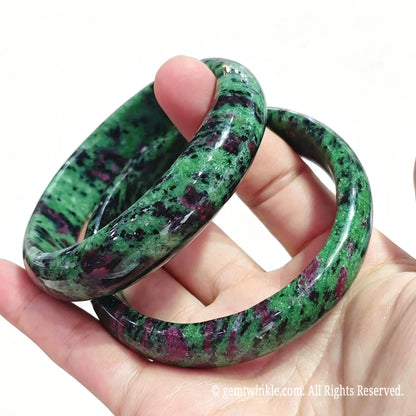 Close up view of natural ruby in zoisite solid bangles held in hand showing dark hornblende inclusions and high gloss finish