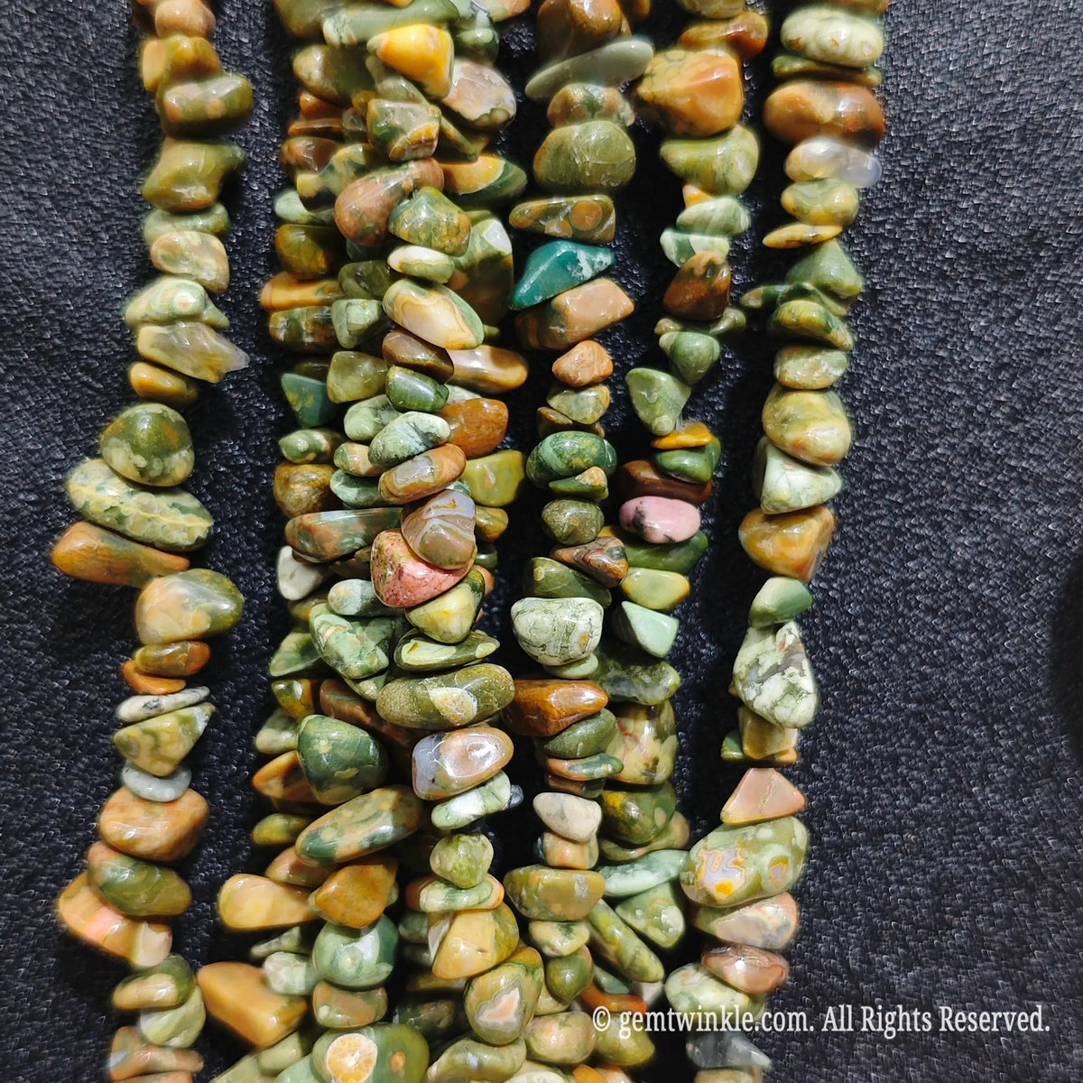 Fingers holding natural rainforest jasper gemstone chip beads on black background