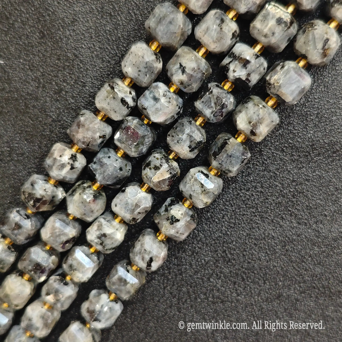 Multiple parallel strands of natural black arfvedsonite soft-tumbled cube beads viewed from distance
