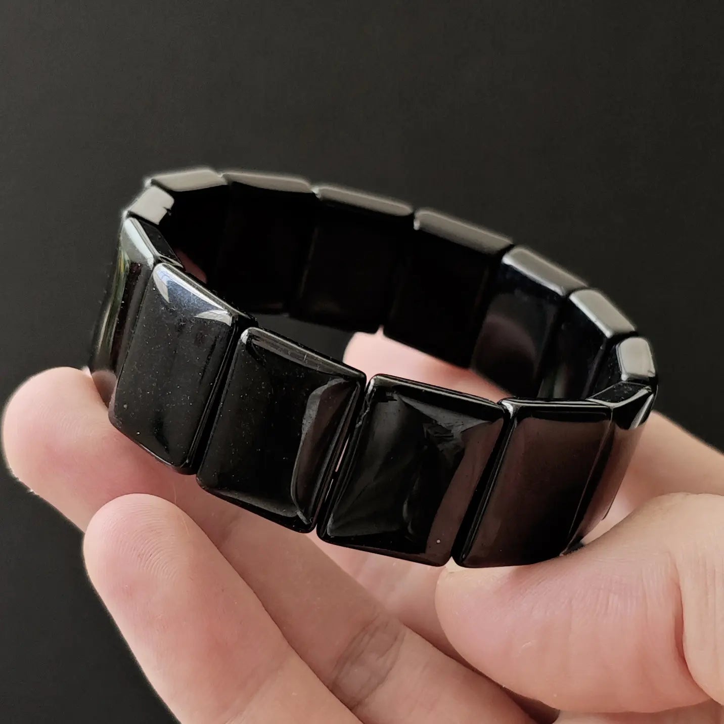 Black obsidian handchain curved in hand next to smartphone for size reference, demonstrating rigidity and structure