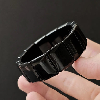Black obsidian square bead handchain held in hand, glossy finish, minimalist design on dark background