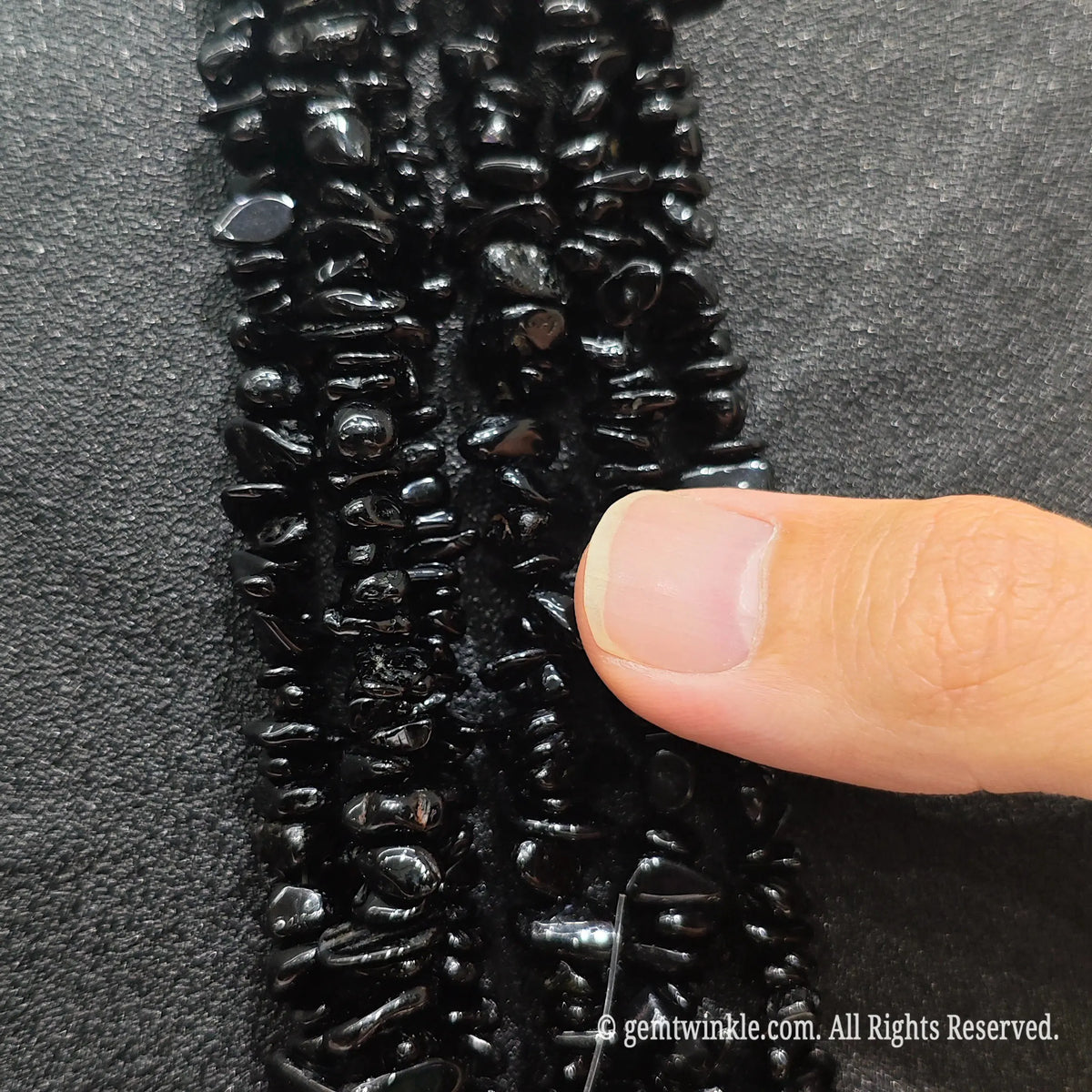 Close up hand holding natural black tourmaline stone chips displaying polished pitch-black surfaces with fine drill holes
