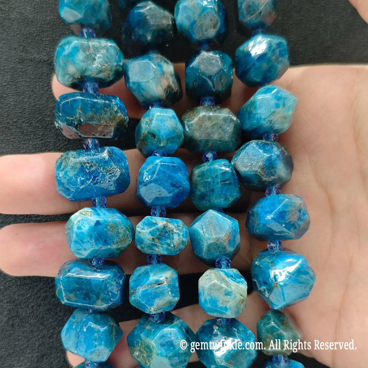 Hand displaying natural blue apatite faceted freeform beads showing vivid teal ocean color and pre-drilled center holes