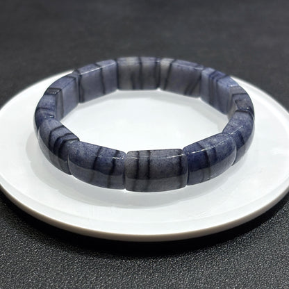 Blue and gray striped bracelet on a white dish with a dark background