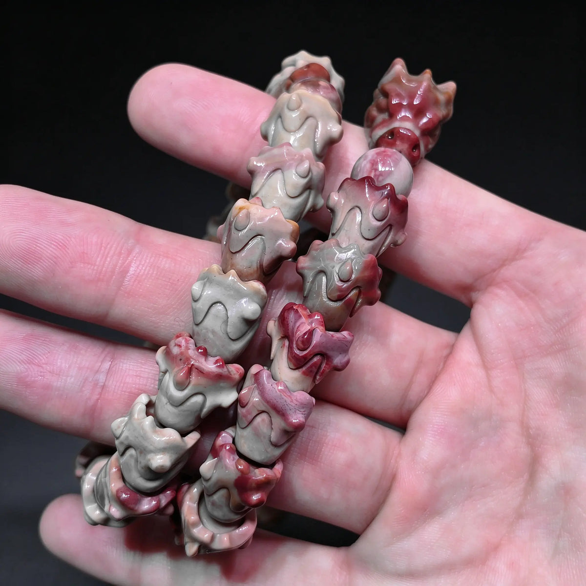 Close up view of two coiled natural multi color Alxa agate dragon spine carved bracelets displaying interlocking vertebrae beads