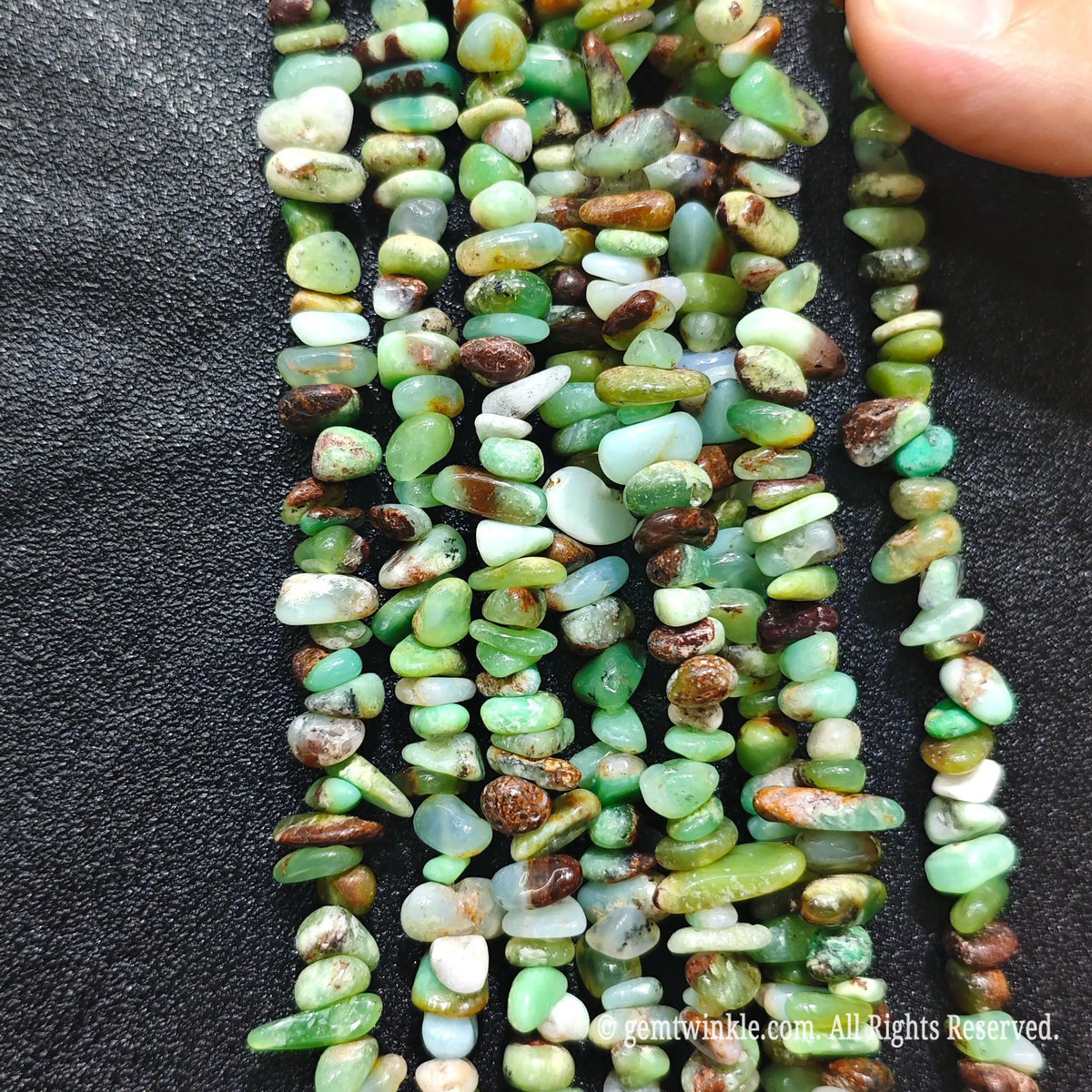Fingers holding translucent apple-green and brown matrix australian jade chip beads on black background