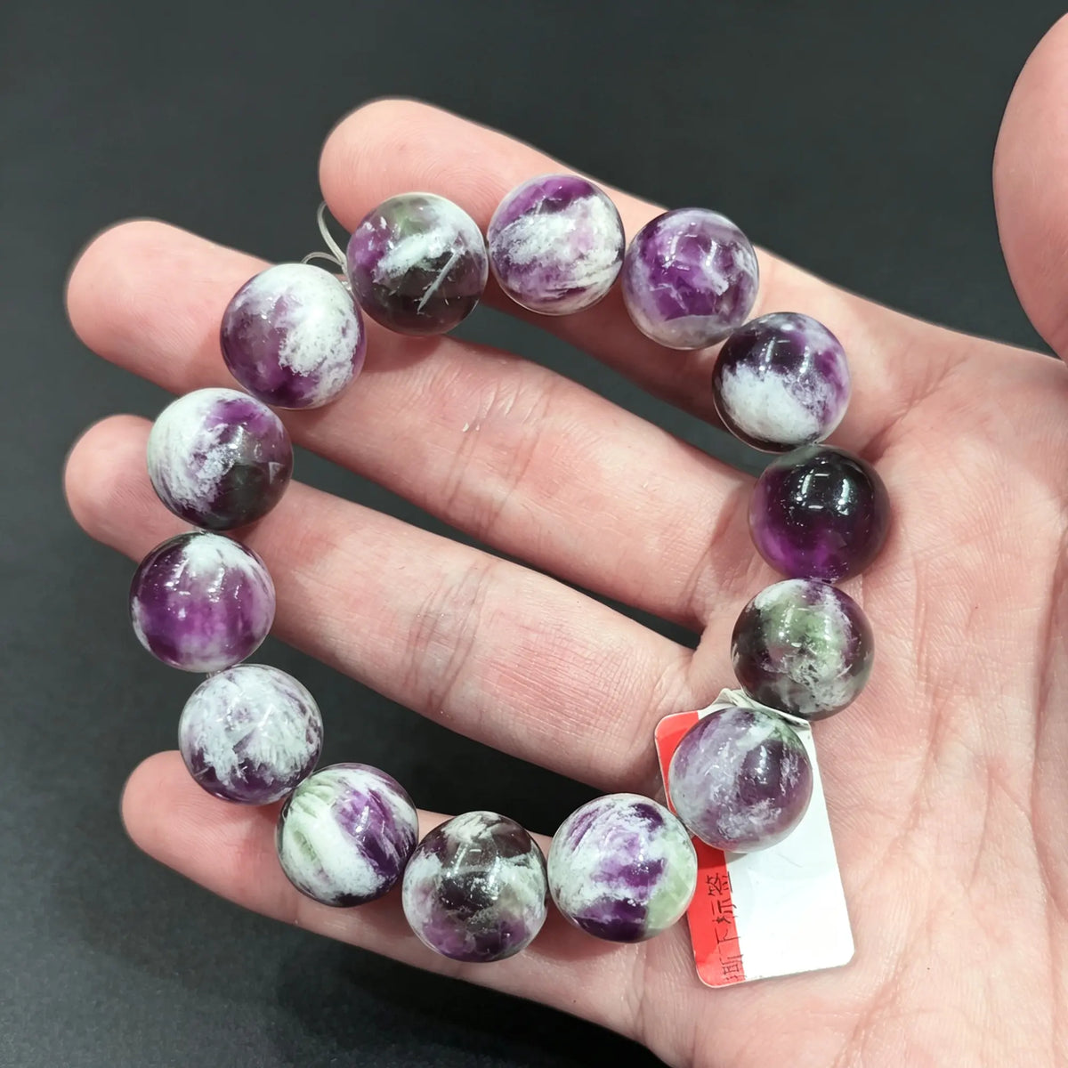 Large natural feather fluorite round bead bracelet displayed on hand showing chunky purple and white inclusions