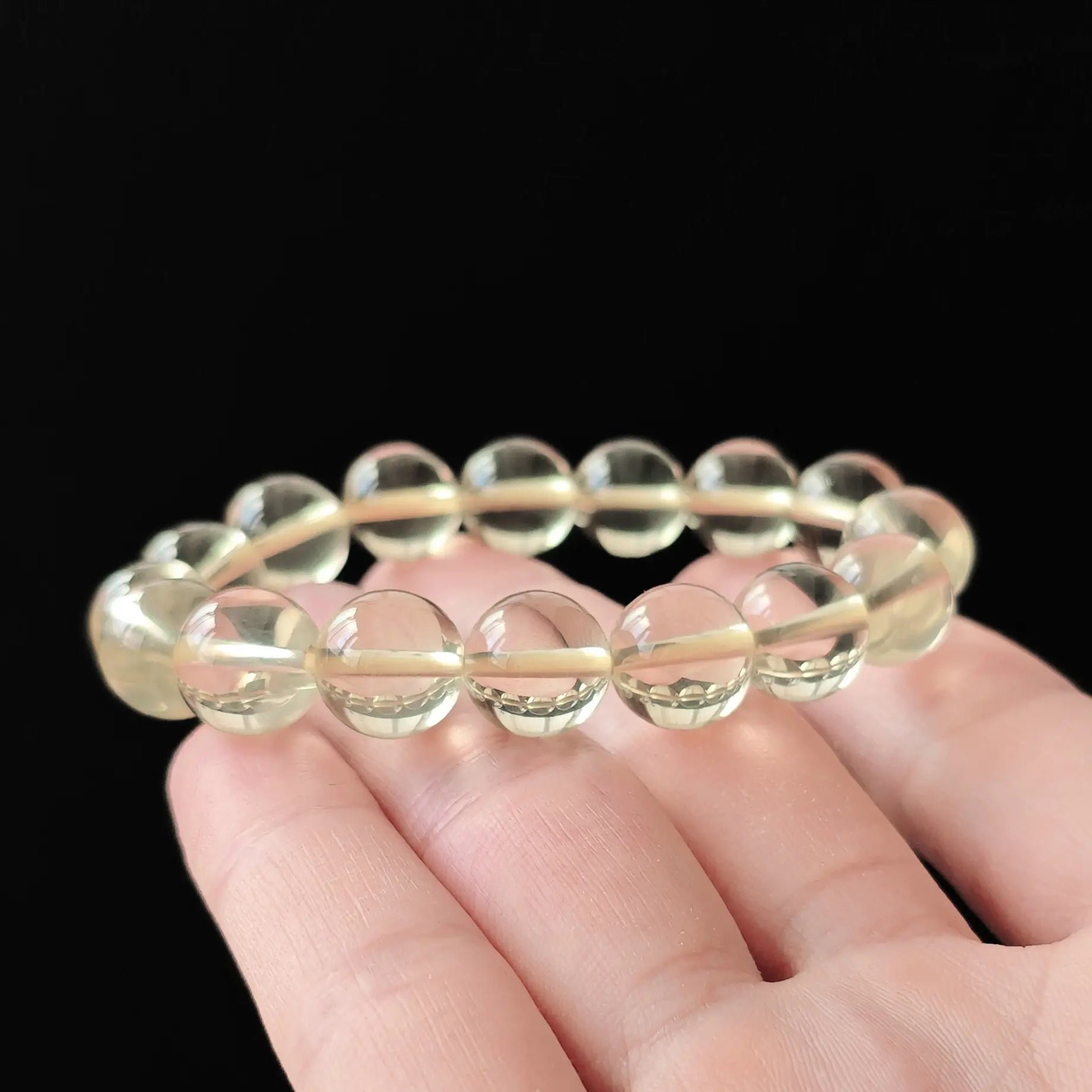 Natural clear lemon citrine round beads (~10mm), high clarity, no inclusions, stretch elastic—held in hand on black background